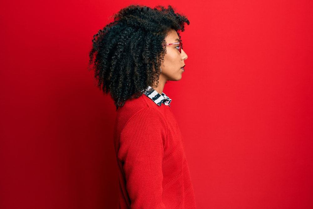 Beautiful African American woman with afro hair wearing sweater and glasses looking to side, relax profile pose with natural face and confident smile.