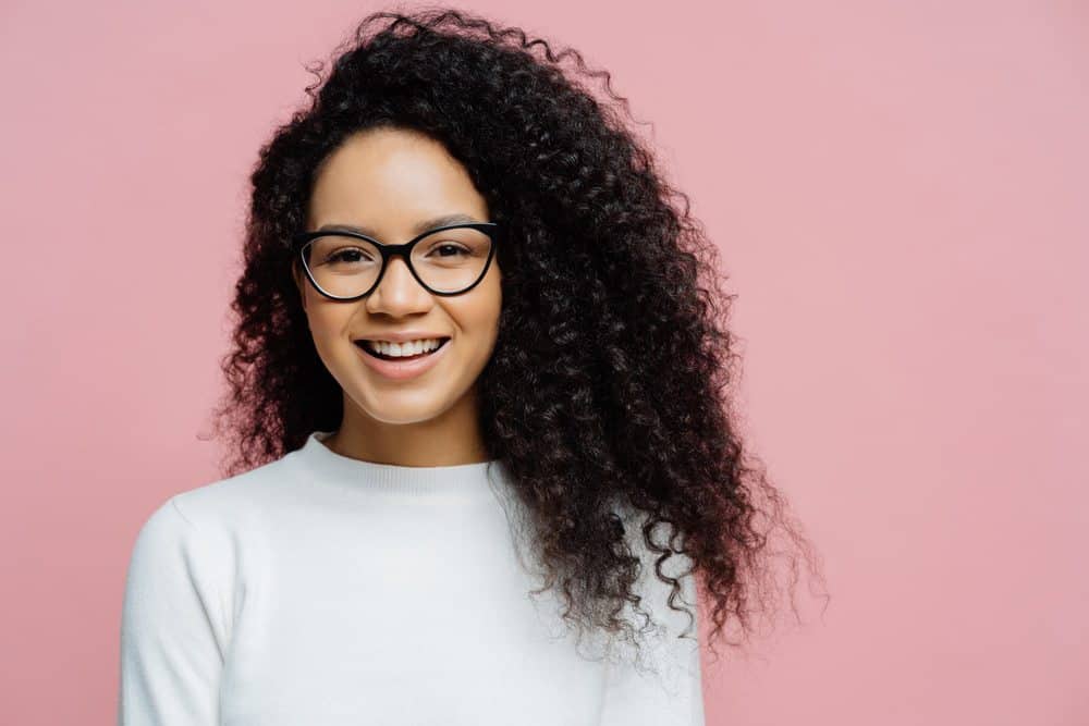 Young African American woman wearing a white sweater with type 3c curly hair strands. Her hair has been treated with bergamot oil.