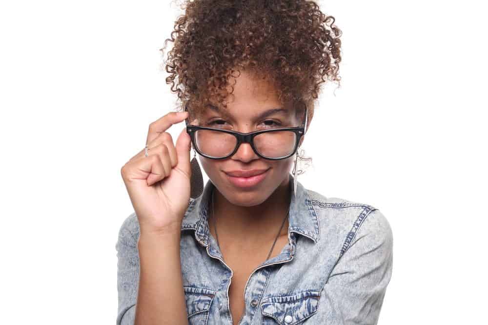 American female wearing black glasses with safflower oil treated curly hair looking directly into the camera while smiling. 