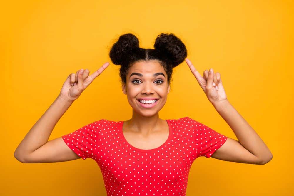 African American lady pointing at her space buns hairdo.