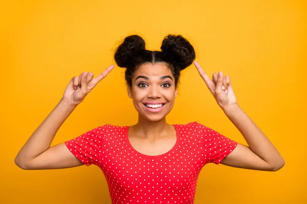 How to Do Space Buns: Easy, Step-by-Step Tutorial for Beginners 2 African American lady pointing at her space buns hairdo.