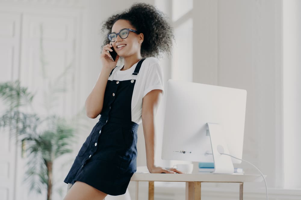 Woman with curly hair talking on the phone in the office drinking Earl Gray tea with bergamot wearing a black dress and white t-shirt.