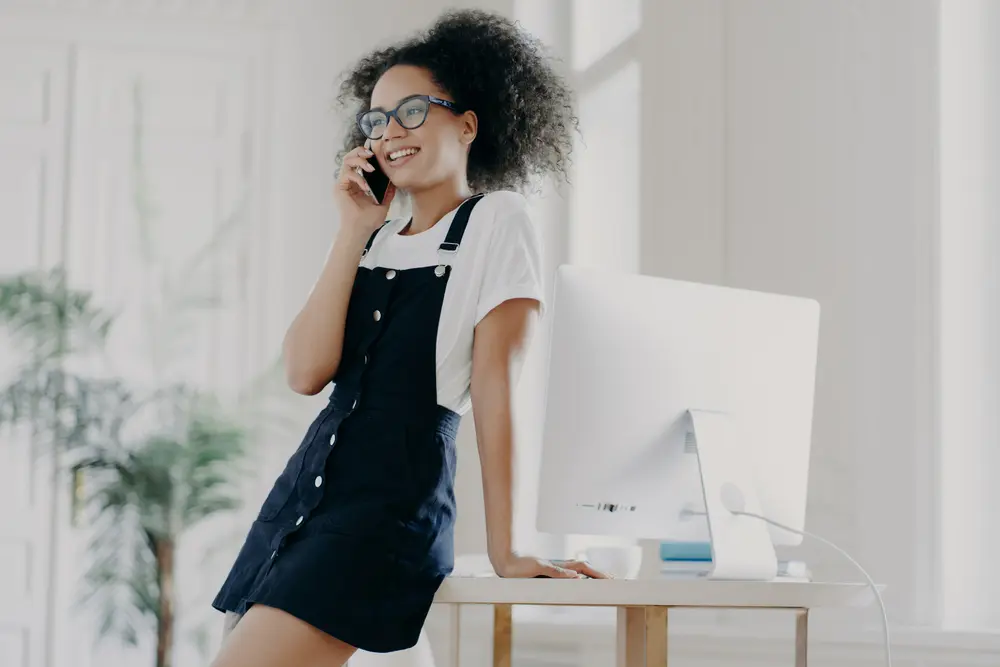 Bergamot Oil: How to Use Bergamot Oil for Hair Growth & More 12 Woman with curly hair talking on the phone in the office drinking Earl Gray tea with bergamot wearing a black dress and white t-shirt.