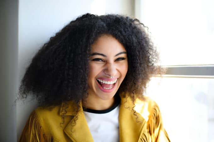 Lady laughing while sitting near a window in a coffee shop with naturally curly hair strands