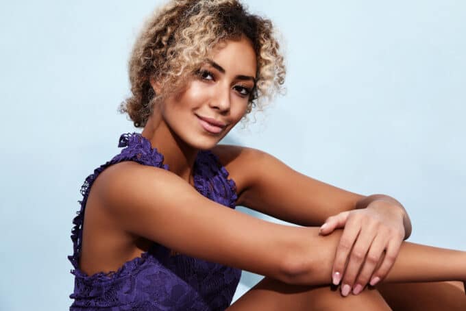 Black woman with wavy hair wearing a purple shirt with lace.