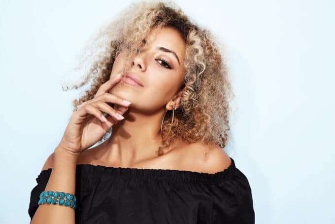 Black lady with a blue beaded bracelet and a black shirt with wavy hair.