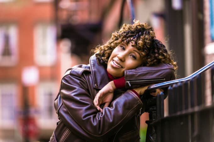 Black girl resting her head on a staircase railing wearing a leather jacket and ombre natural hair