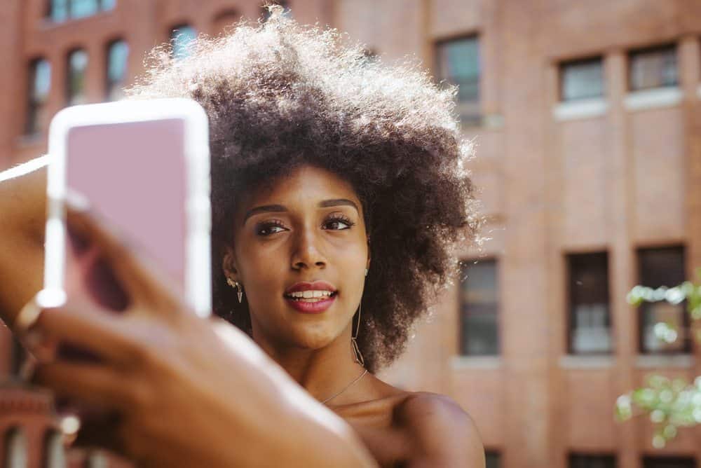 Black girl with natural hair taking a selfie with her mobile phone.