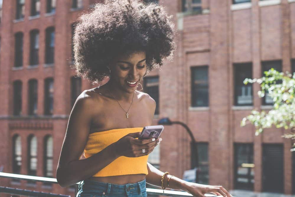 Black girl with 4D hair wearing a silver necklace and a yellow crop top, beaded bracelet and blue jeans. 