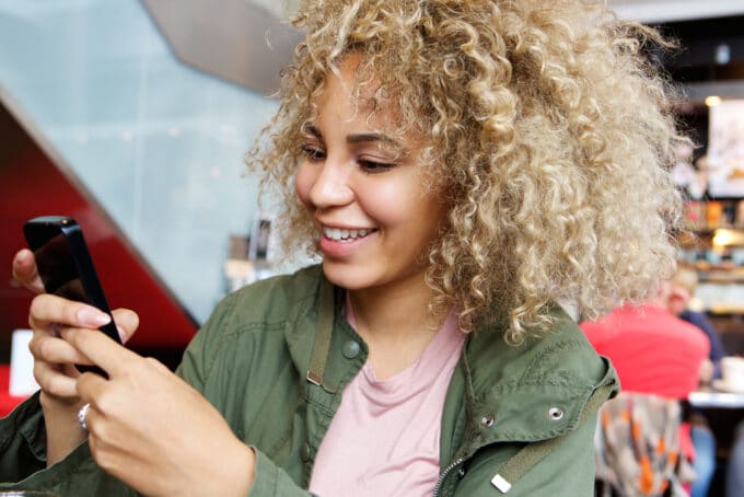 Mixed race female wearing ombre curly hair and a green jacket using an iPhone.