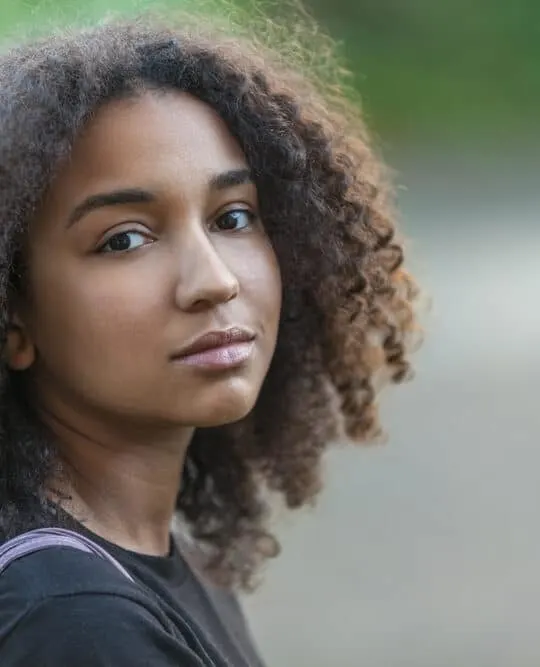 Outdoor portrait of beautiful mixed race African American female with hair that's been treated with coconut oil for hair growth and scalp care.