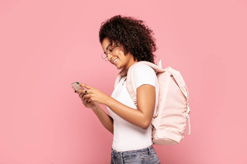 African American female with type 3 curly hair wearing a white t-shirt and a pink backpack.