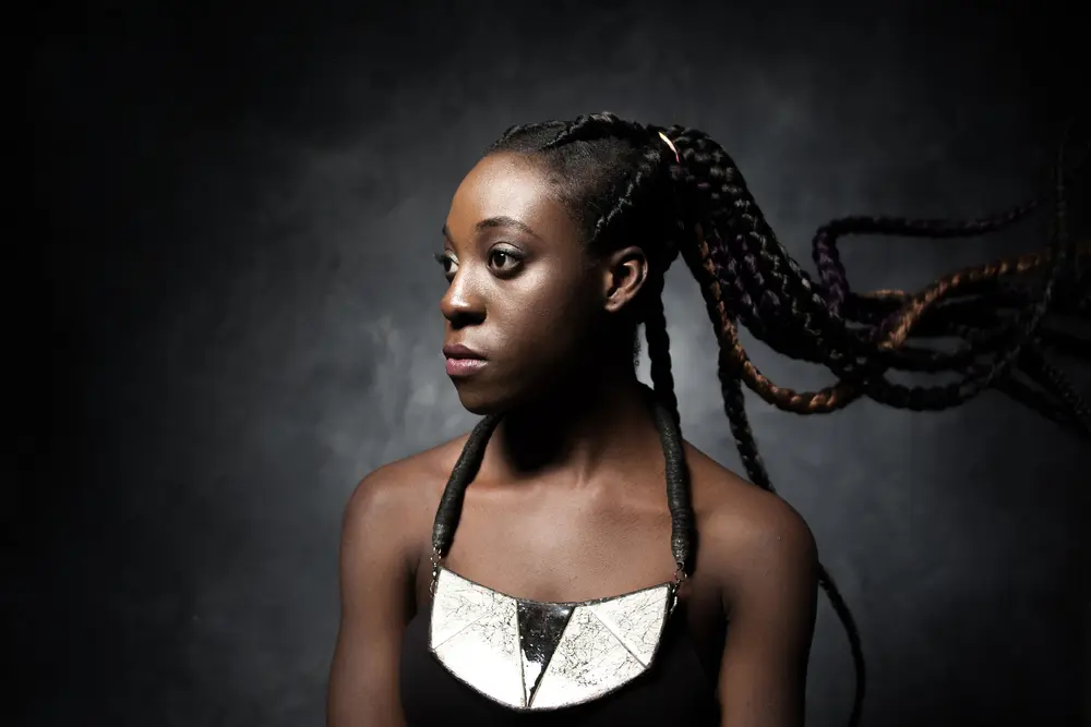 Ghana Braids: How to Do Ghanaian Cornrow Braid Hairstyles for Beginners 7 Black female looking into the distance, wearing a black dress.