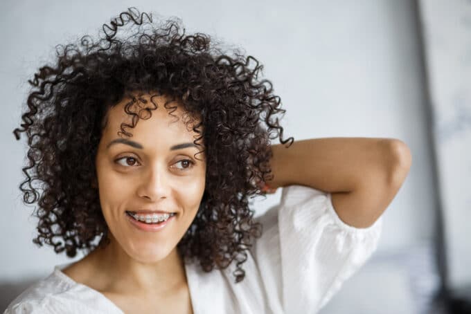 Black lady with braces rubbing her hands through her type 3c naturally curly hair strands.