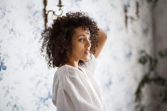 Black woman looking in the mirror rubbing her type 3c curly hair.