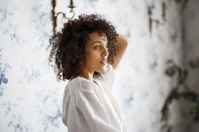 Do I Need a Wig Stand? How to Make a DIY Wig Stand at Home 14 Black woman looking in the mirror rubbing her type 3c curly hair.