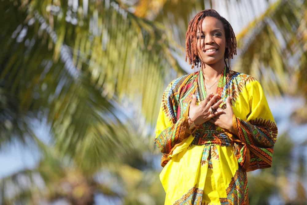 A black woman after having yarn locs (or faux locs) installed wearing a yellow multi-colored shawl and silk scarf.