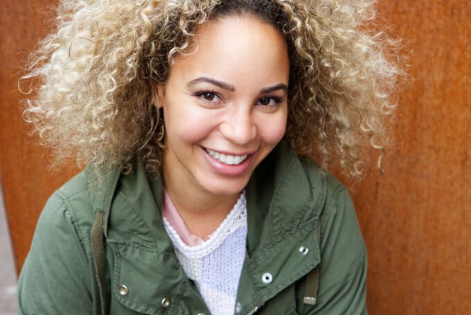 Black woman with a huge smile with hair that's been dyed blonde. 