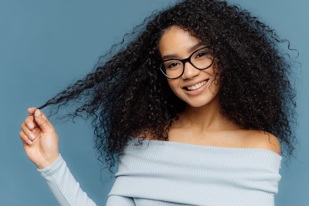 African American woman naturally curly type 3a hair that's been treated with bergamot oil for hair growth wearing a blue sweater and reading glasses.