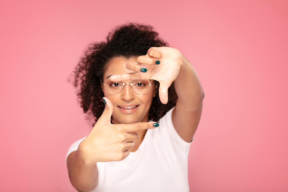 African American female wearing a white t-shirt, green fingernail polish, and curly hair.