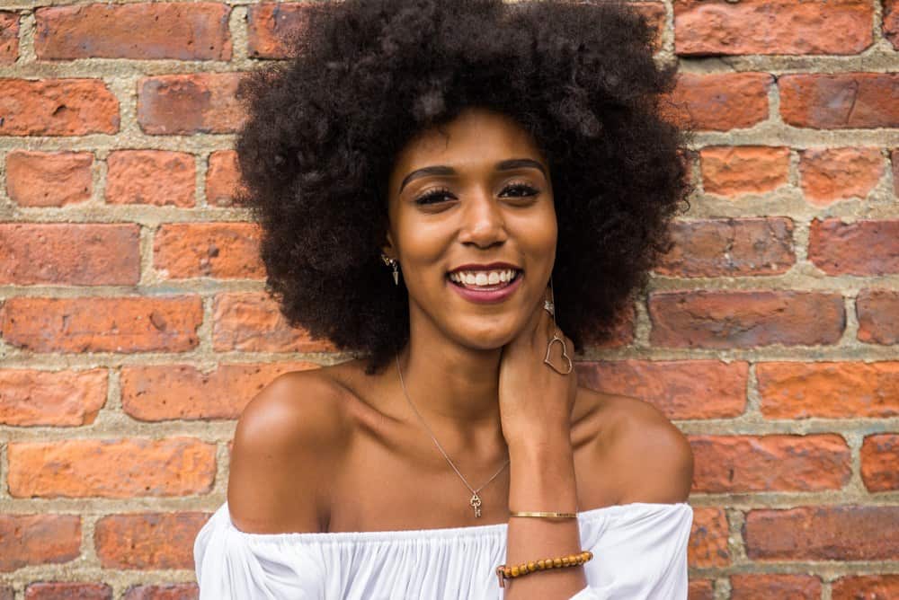 Smiling African American woman wearing a necklace holding a key with naturally curly hair.