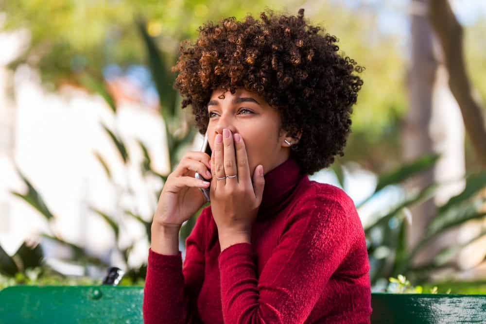 Young African American woman speaking on mobile phone with ombre naturally curly hair wearing read shirt.