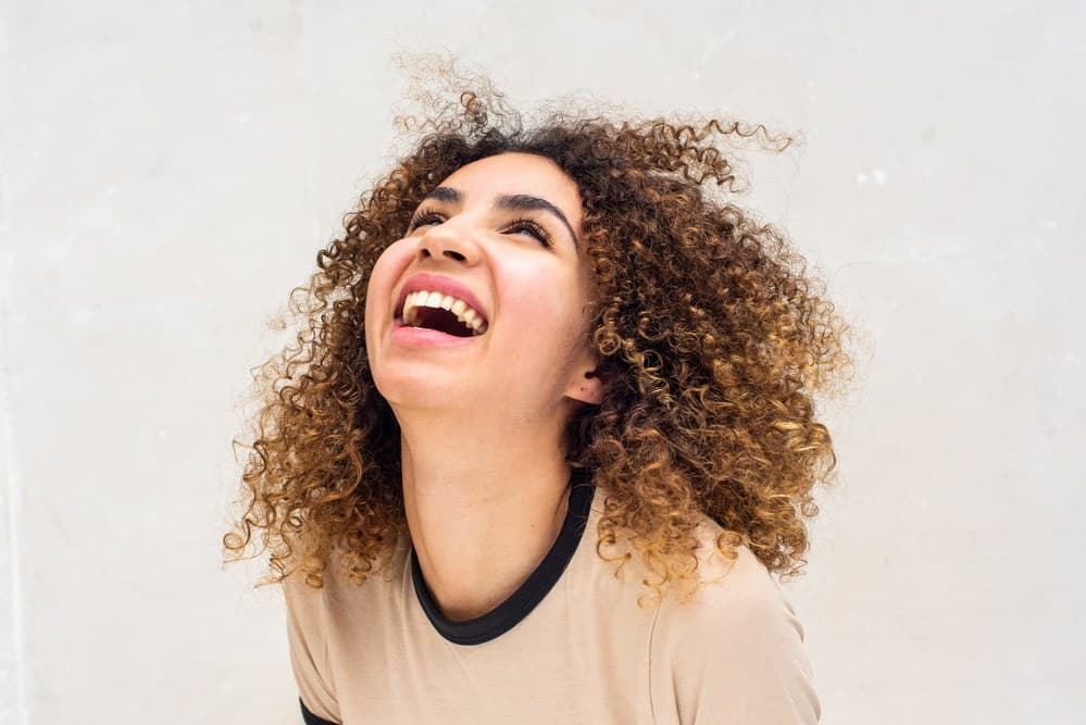 Women with naturally curly hair with a huge smile wearing a badge t-shirt.