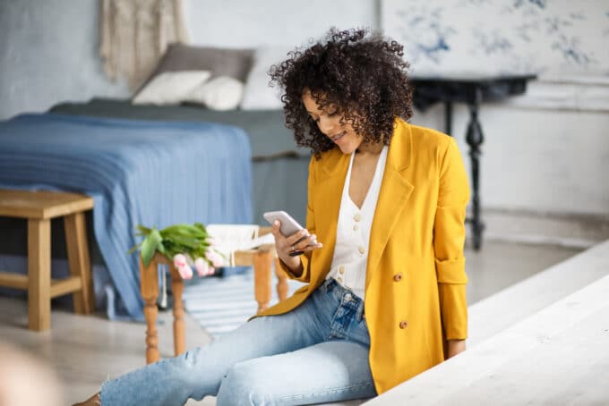 Lady with an orange jacket sitting in her bedroom.