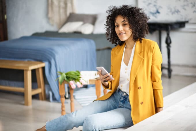 African American lady with naturally curly type 3c hair wearing an orange sports coat, white t-shirt and blue jeans.