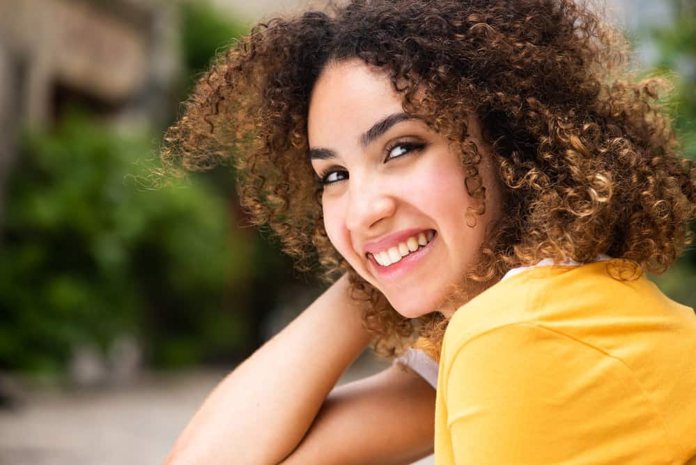 African American female wearing a yellow t-shirt with a type 3b curl pattern.