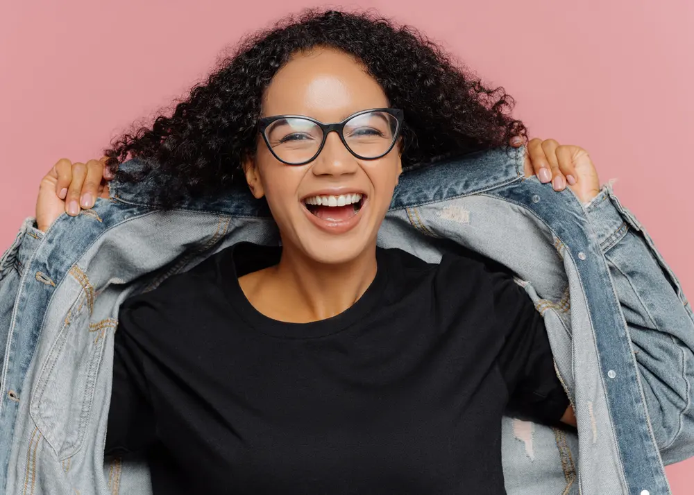 Bergamot Oil: How to Use Bergamot Oil for Hair Growth & More 7 Back lady with a huge smile wearing a blue jean jacket and type 3B curly hair with a black undershirt.
