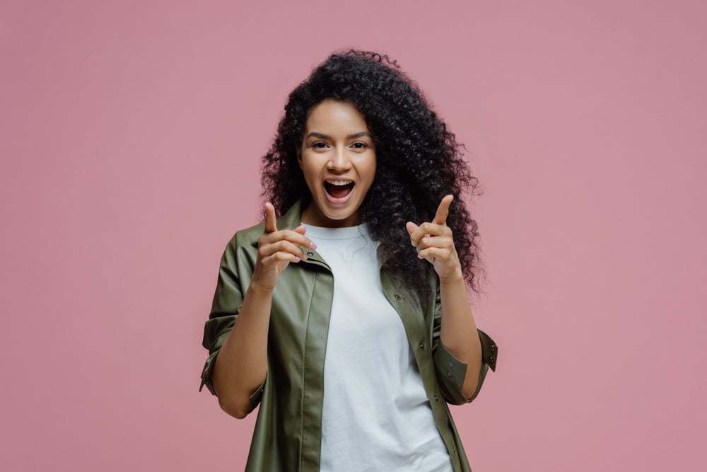 Happy black women pointing towards the camera wearing a green shirt and white t-shirt.