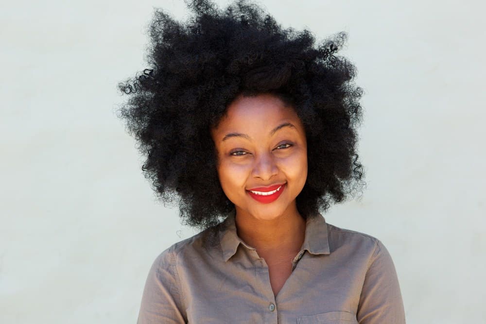 Black woman with curly hair wearing red lipstick and gray collared dress shirt.