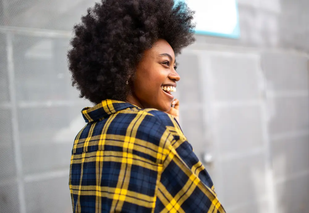 How To Grow Natural Hair Faster: Grow Hair Fast Step-by-Step 13 Smiling young back girl wearing a yellow and blue shirt.