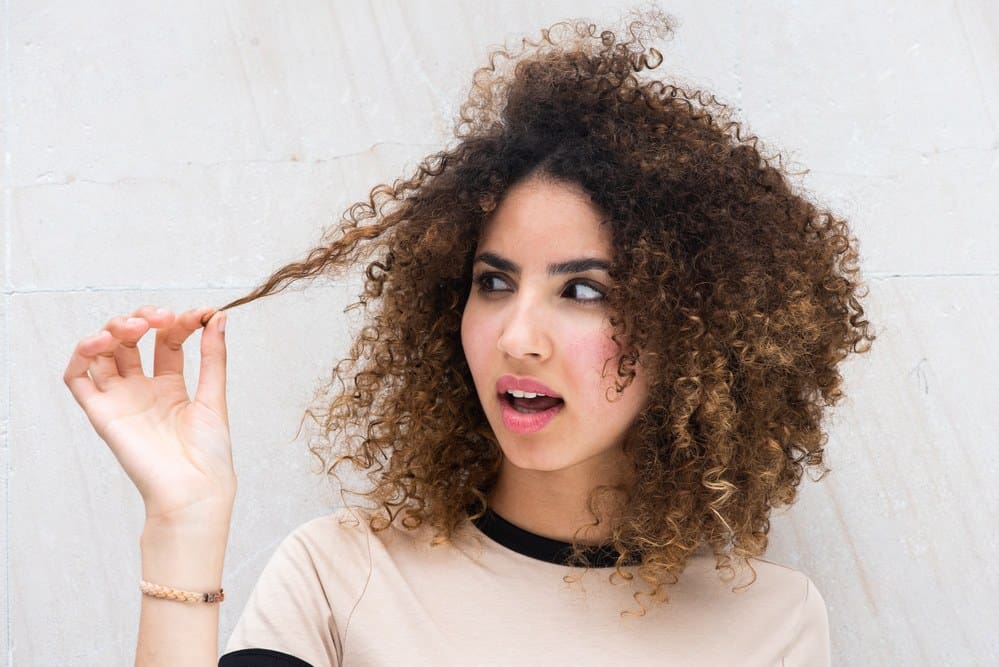 Black woman with type 3b curly hair holding her hair strand after using the squish to condish method with flax-seed gel.