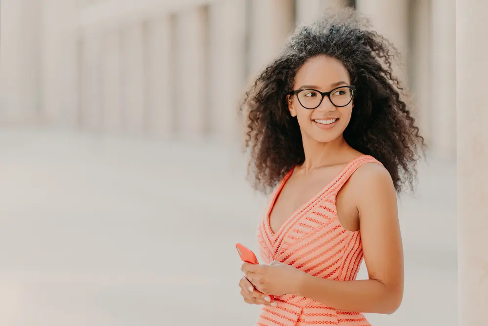 Bergamot Oil: How to Use Bergamot Oil for Hair Growth & More 10 Young girl wearing a pink stripped dress texting friends on an iPhone with type 3a wavy hair.