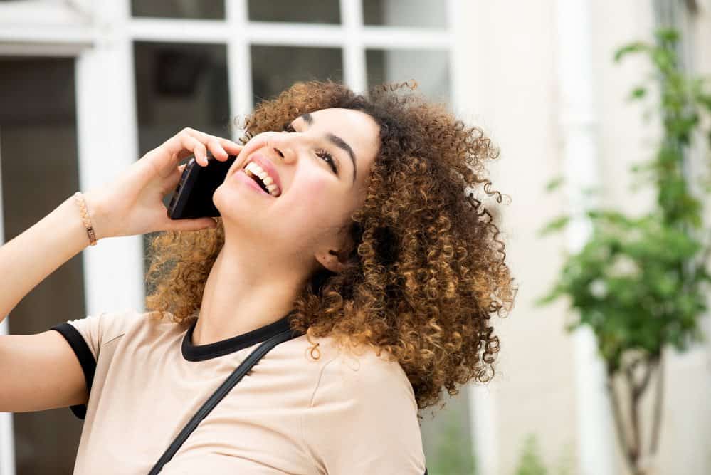 Black women with naturally curly hair talking on a cell phone outside.