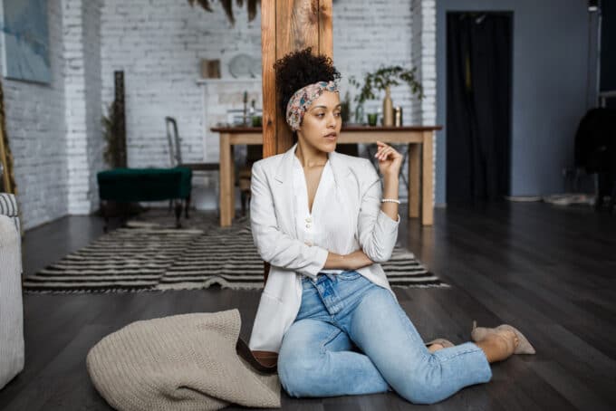 Light-skinned black woman wearing a white sports coat, blue jeans, and beige high heels.