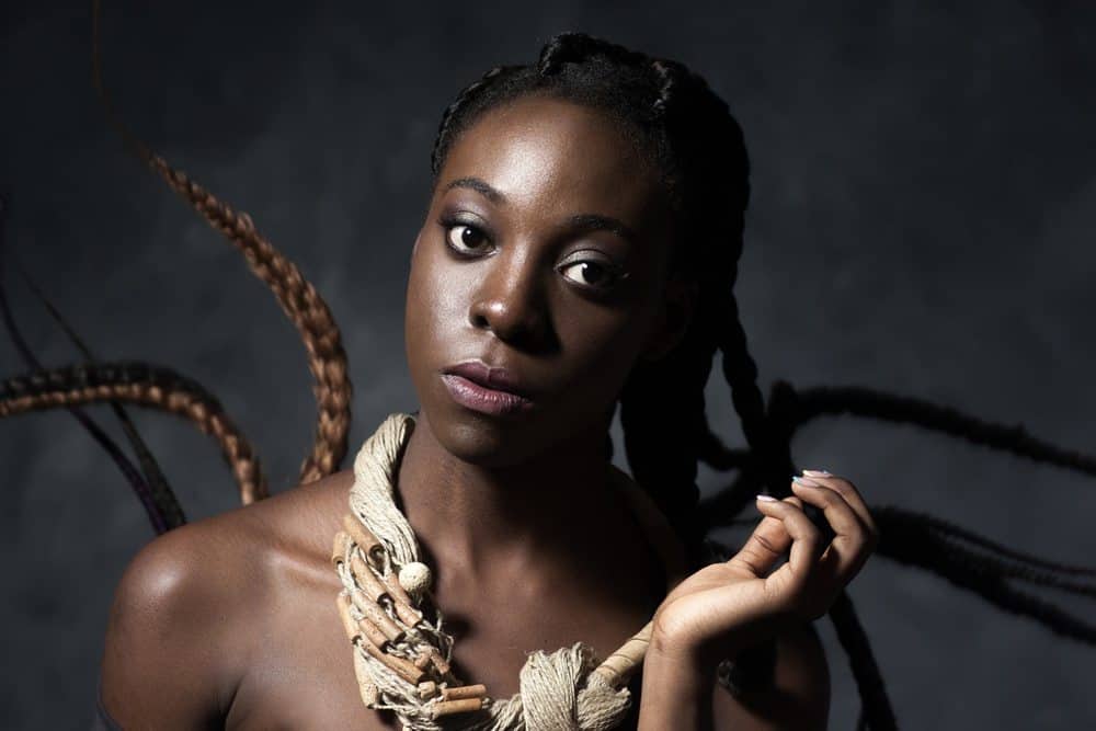 Black women looking directly into the camera wearing a wooden necklace.