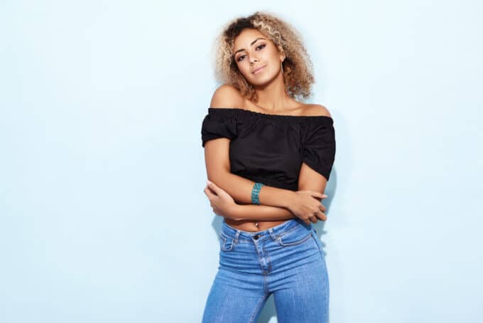 African American female with blonde curly hair wearing a black shirt and blue jeans.