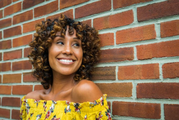 Beautiful African American female with Shirley Temple curls leaning against a brick wall