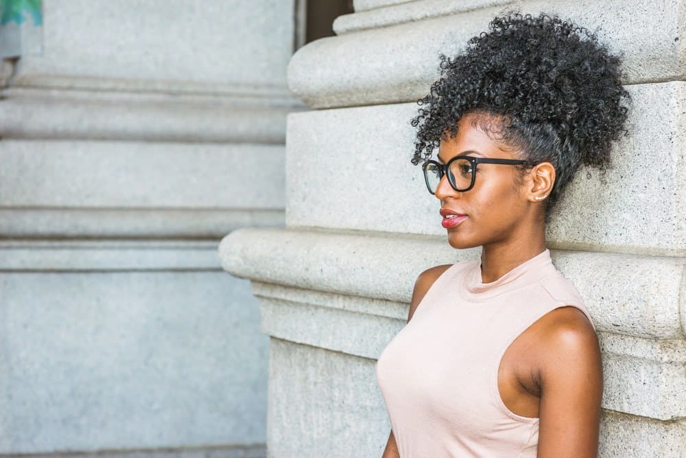 African American women with 4A natural hair thinking about the origin of black seed oil while leaning on a stone wall.