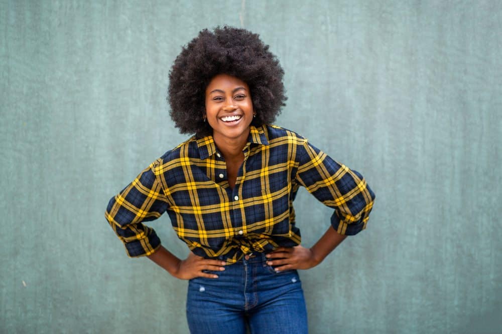 Black female with her hands on her hip wearing a plaid shirt.