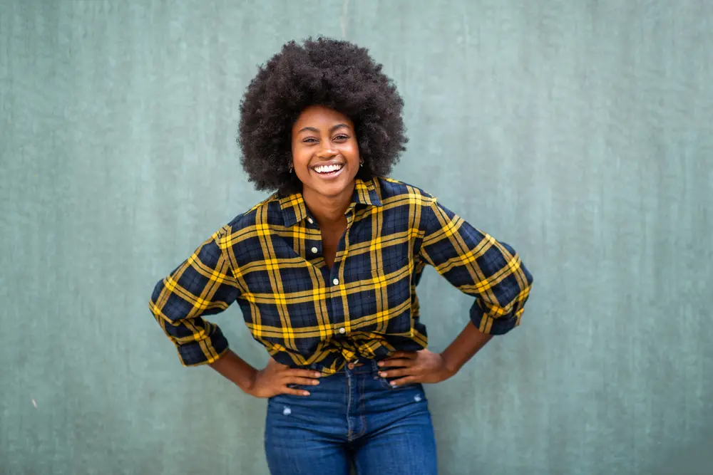 How To Grow Natural Hair Faster: Grow Hair Fast Step-by-Step 11 Black female with her hands on her hip wearing a plaid shirt.
