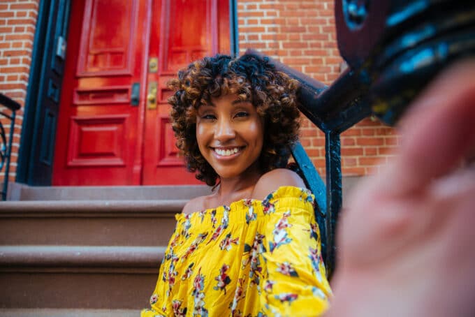 American women wearing a yellow off the shoulder shirt, natural lipstick, and bouncy curls