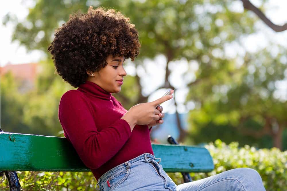 Black girl ordering a good moisturizer from Target's website while sitting on a green wood park bench.