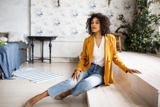 African American female posing for a photo in her bedroom wearing cut-off blue jeans and orange coat.