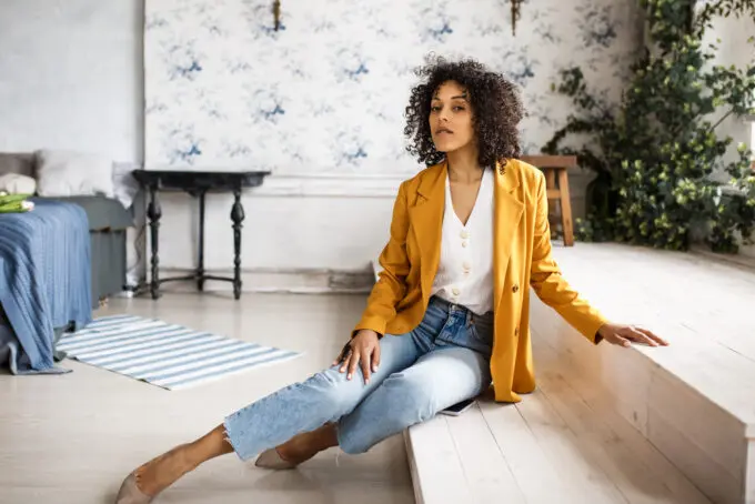 Do I Need a Wig Stand? How to Make a DIY Wig Stand at Home 13 African American female posing for a photo in her bedroom wearing cut-off blue jeans and orange coat.