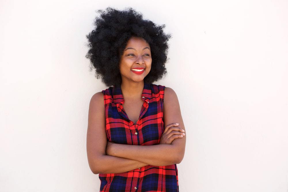 Black girl wearing a red and blue plaid casual shirt with her arms folded