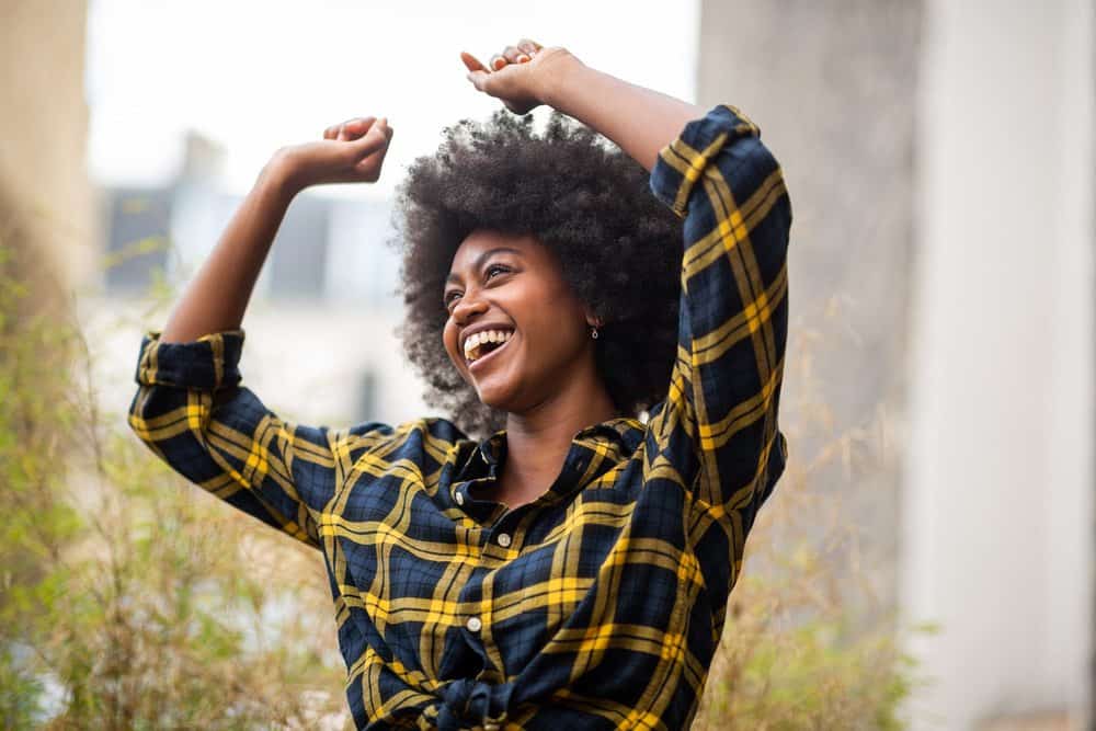 Cheerful woman with her arms raised in the air while dancing outdoors.